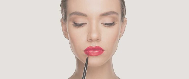 Beautiful woman applying red lipstick to show off lip injections by APT Medical Aesthetics