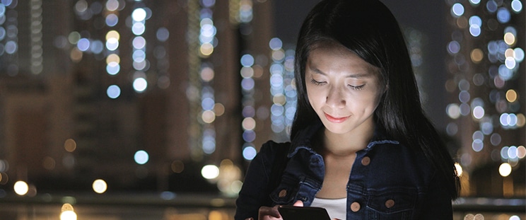 A woman stares at her illuminated phone screen at night