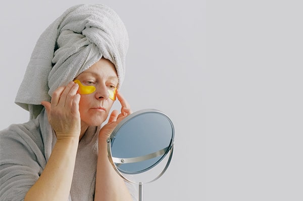 An older woman applies under-eye masks in the mirror